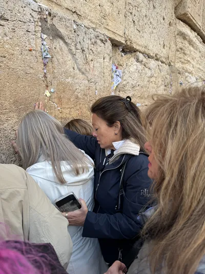 People praying with hands and foreheads against a stone wall
